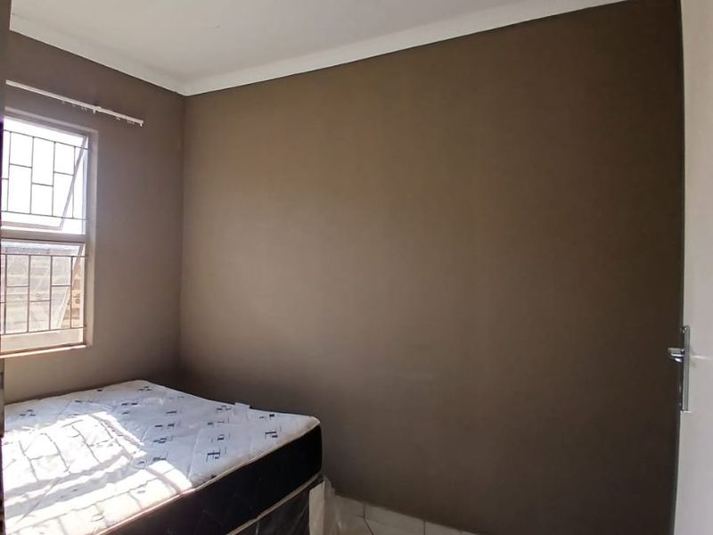 A compact bedroom featuring tiled flooring, a window with security bars, and a ceiling-mounted light fixture.