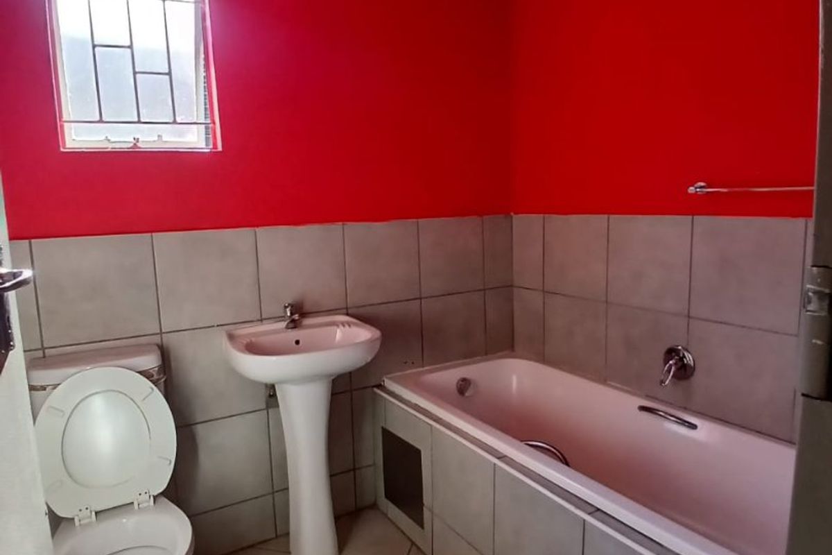 A functional bathroom featuring a pedestal basin, built-in bathtub, and toilet, with tiled flooring and wall splashbacks. The space would benefit from cosmetic updates.