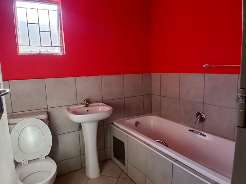 A functional bathroom featuring a pedestal basin, built-in bathtub, and toilet, with tiled flooring and wall splashbacks. The space would benefit from cosmetic updates.