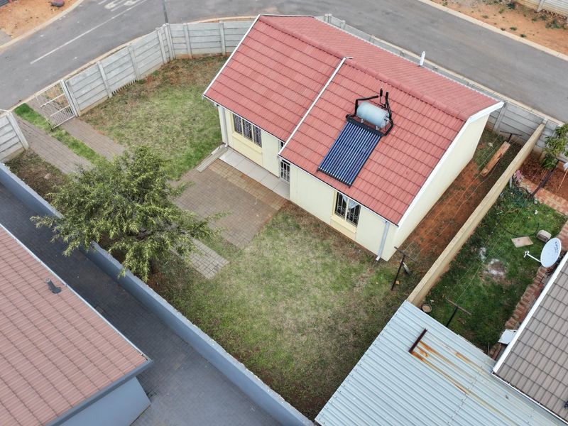 Aerial view of a residential property featuring a tiled roof with a solar water heating system, a private garden, and paved patio area.