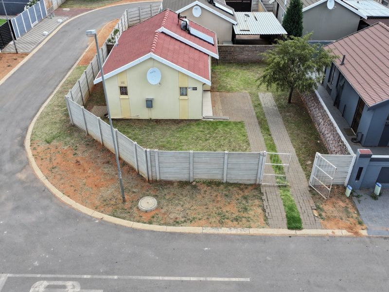 Aerial view of a residential property featuring a tiled roof, solar water heater, paved walkway, and enclosed garden area within a suburban estate.