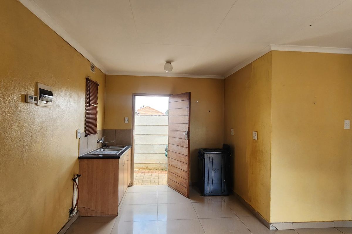 A compact, empty kitchen area featuring tiled flooring, basic cabinetry with a sink, and direct access to the exterior.