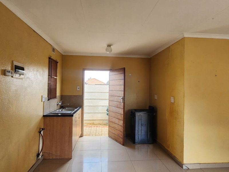 A compact, empty kitchen area featuring tiled flooring, basic cabinetry with a sink, and direct access to the exterior.
