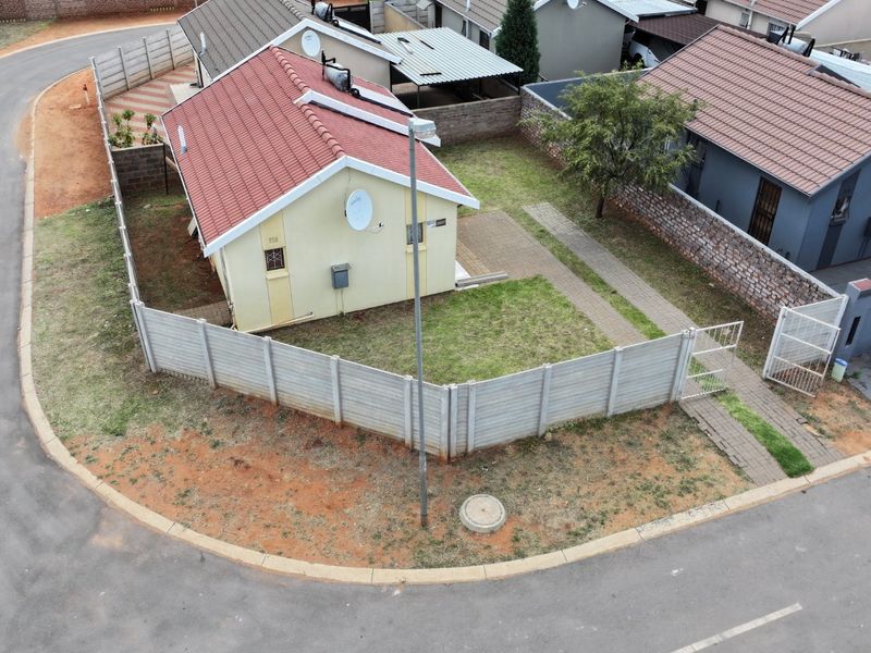 Aerial view of a residential property featuring a tiled roof house, enclosed by a precast concrete boundary wall with a paved walkway and garden area.