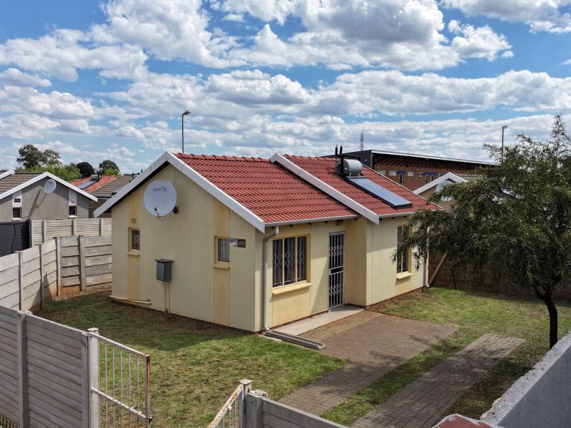 A detached single-story house featuring a tiled roof, solar water heating system, paved driveway, and secure perimeter walling in a residential setting.
