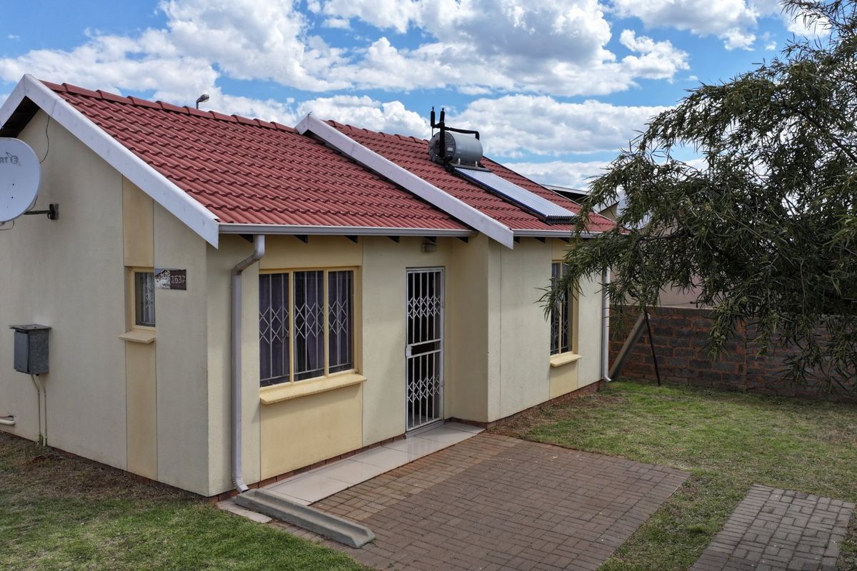Rear view of the house featuring a tiled roof, solar water heater, paved patio area, and secure window bars.