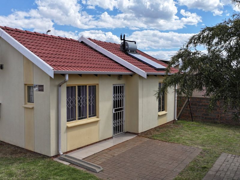 Rear view of the house featuring a tiled roof, solar water heater, paved patio area, and secure window bars.