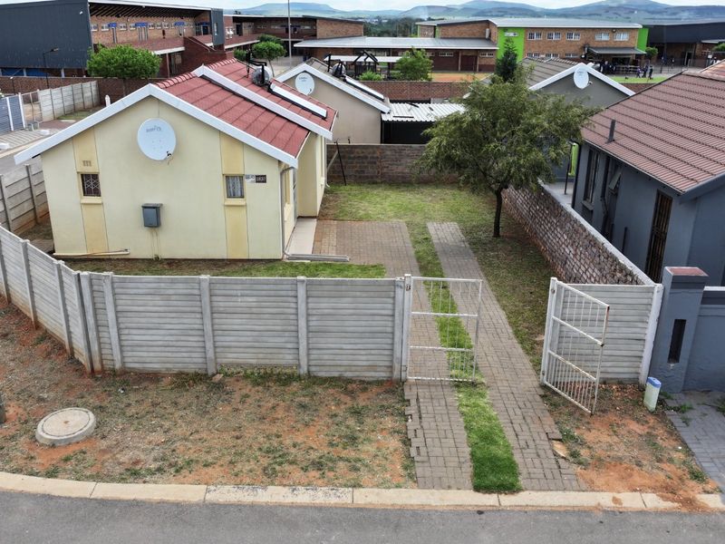 Aerial view of a residential property featuring a paved driveway, precast concrete boundary walls, and a tiled roof house with a small garden.