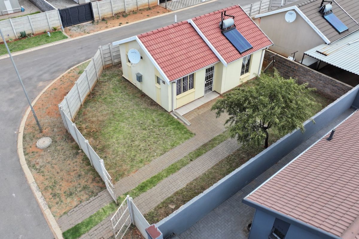 Aerial view of a detached house featuring a tiled roof with solar water heating, a paved driveway, and a private garden enclosed by precast walls.