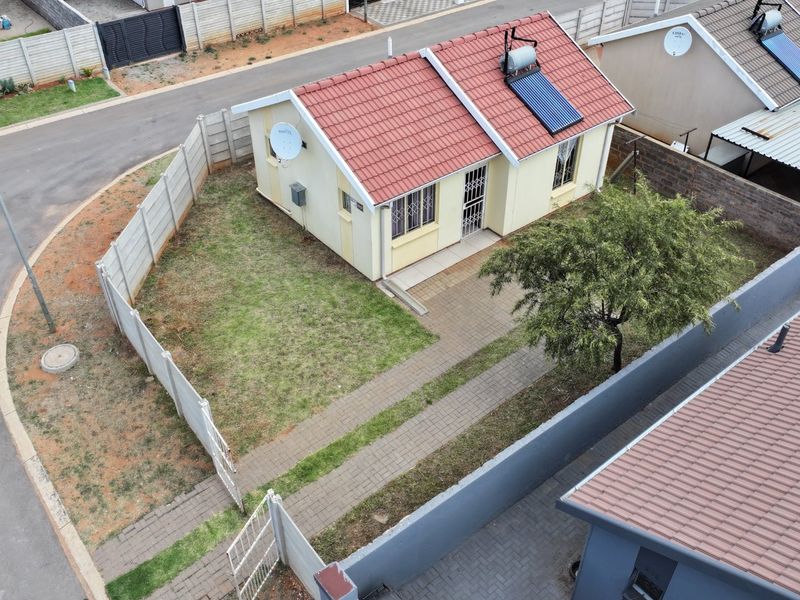 Aerial view of a detached house featuring a tiled roof with solar water heating, a paved driveway, and a private garden enclosed by precast walls.