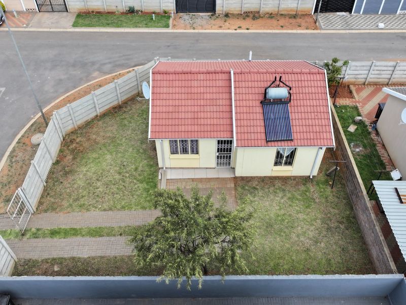 Aerial view of a detached house featuring a tiled roof with a solar water heater, a private garden, and a paved driveway.