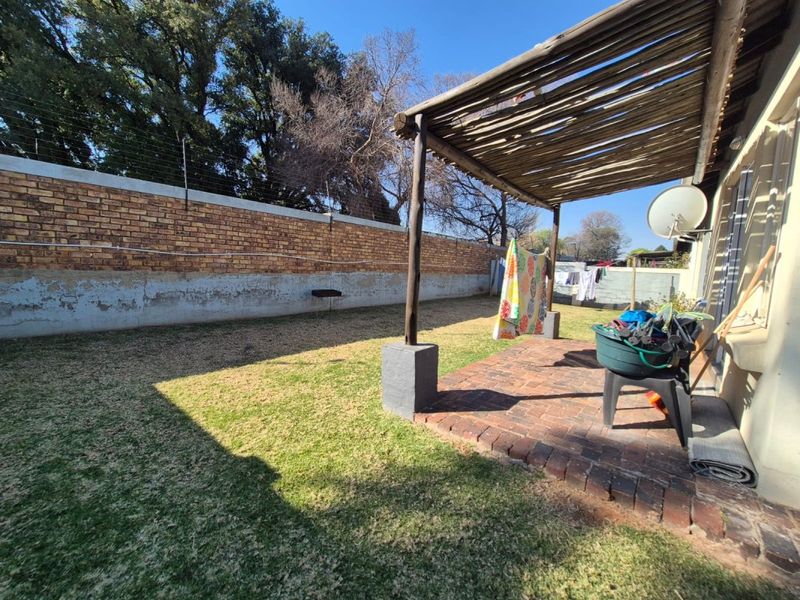 A rear garden area featuring a brick-paved patio with a timber pergola, enclosed by a perimeter brick wall with electric fencing.
