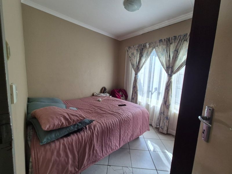 A compact bedroom featuring tiled flooring and a window with security bars, requiring some maintenance to the flooring.