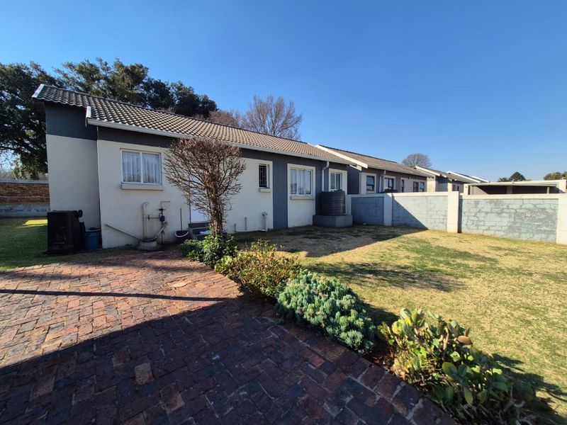 Rear view of the property featuring a brick paved area, a small garden, a water tank, and a secure boundary wall.