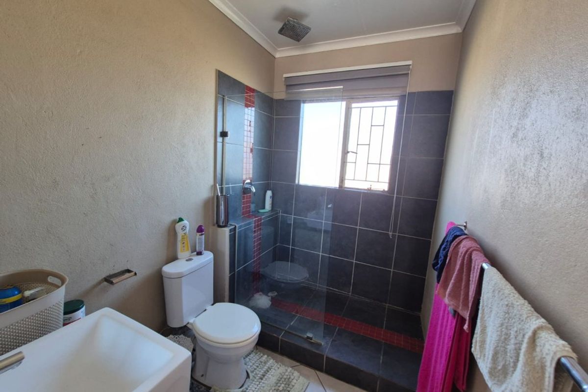 A functional bathroom featuring a walk-in shower with glass screen, wall-mounted basin, and toilet, finished with dark wall and floor tiling.