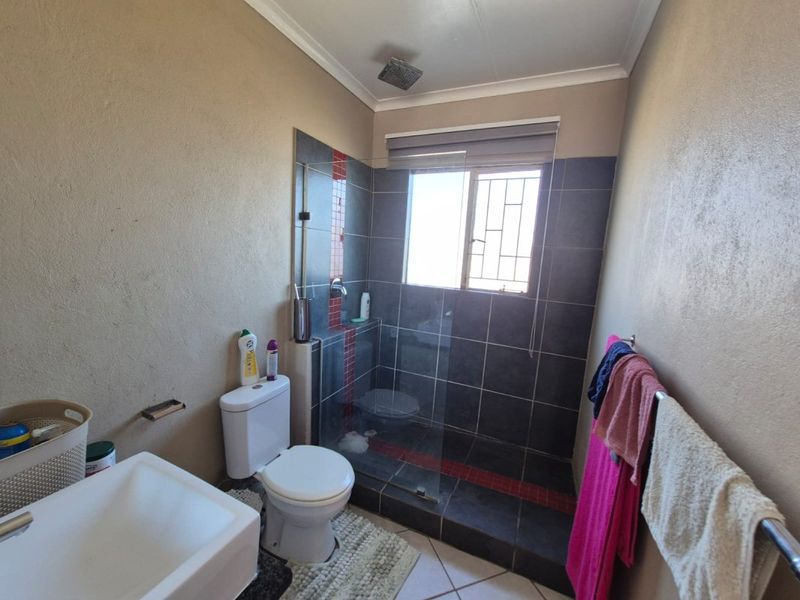 A functional bathroom featuring a walk-in shower with glass screen, wall-mounted basin, and toilet, finished with dark wall and floor tiling.