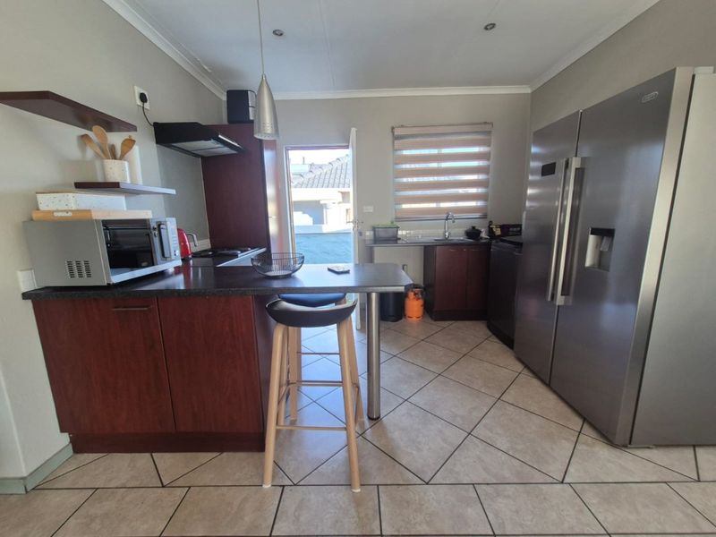 A functional kitchen featuring dark wood cabinetry, laminate countertops, tiled flooring, and direct access to the exterior.