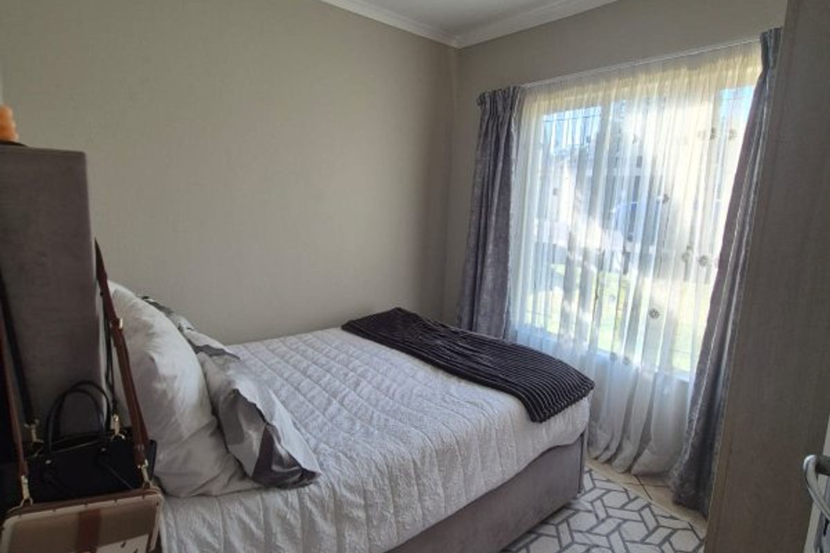 A cozy bedroom featuring tiled flooring, neutral wall tones, and natural light through a window with curtain rails.