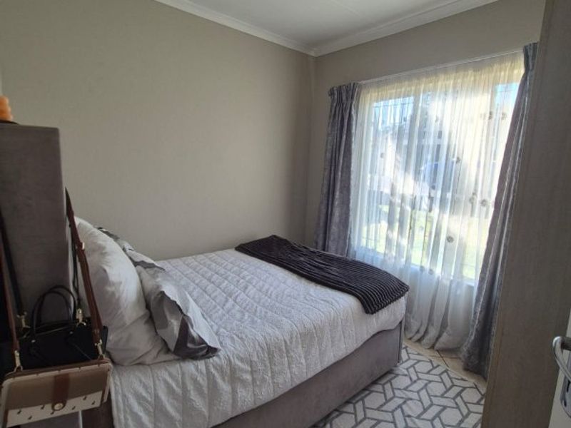 A cozy bedroom featuring tiled flooring, neutral wall tones, and natural light through a window with curtain rails.