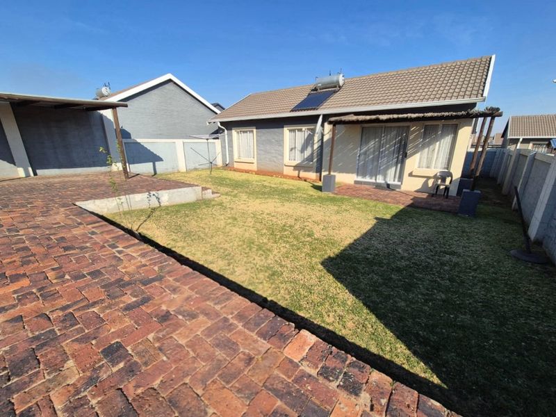 Rear view of the property featuring a paved patio area, a small lawn, and a solar water heating system installed on the tiled roof.