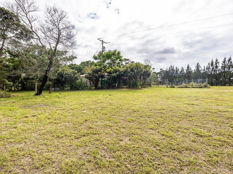 A spacious, open grassed area on a farm property, featuring mature trees, perimeter fencing, and an overhead utility pole.