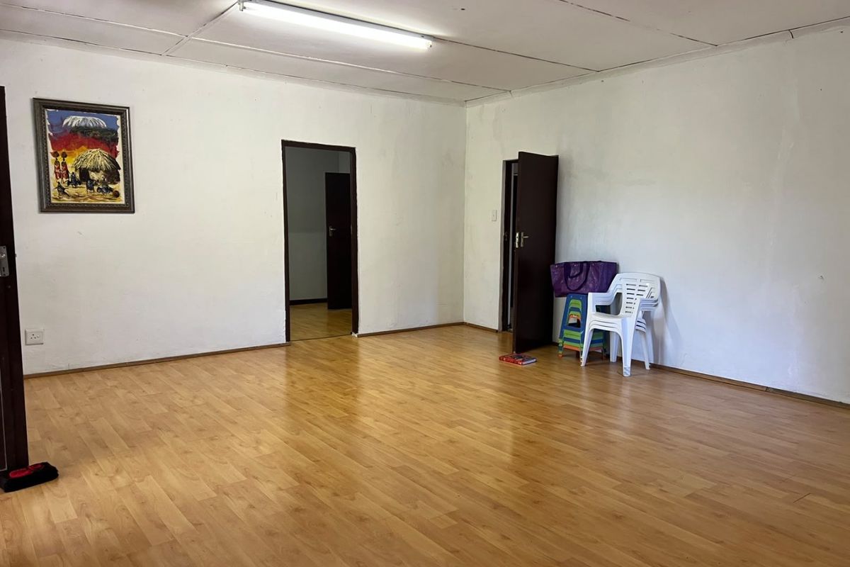 A spacious, empty living area featuring laminate flooring and a tiled ceiling, offering a blank canvas for interior design updates.