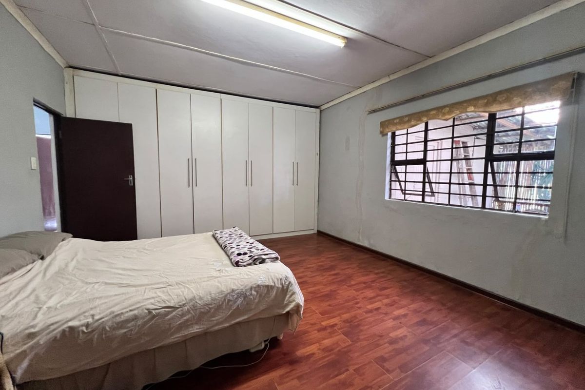 Spacious bedroom featuring built-in cupboards, laminate flooring, and security bars on the window. The room requires cosmetic updates to address wall condition.