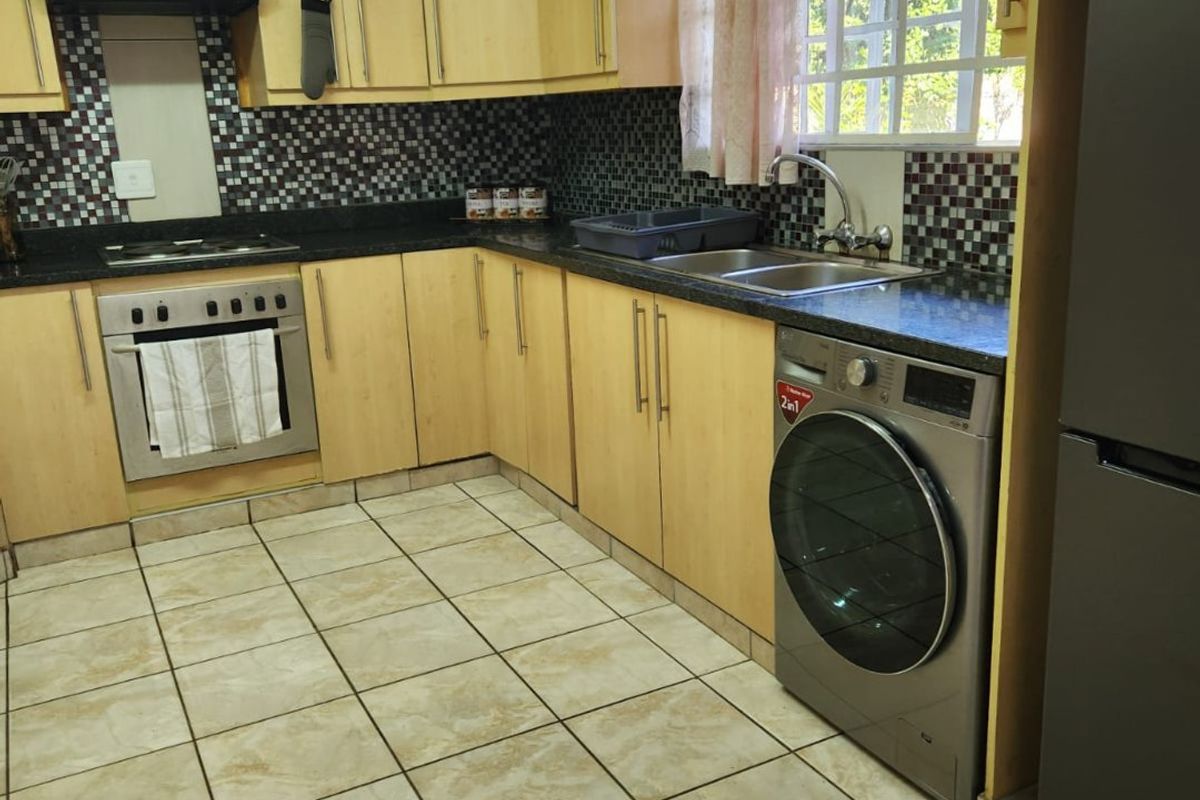 A functional kitchen featuring light wood cabinetry, mosaic tile backsplash, tiled flooring, and integrated appliances including an oven and extractor fan.