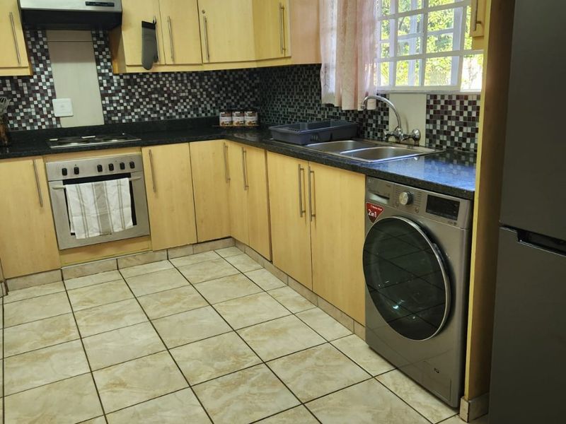 A functional kitchen featuring light wood cabinetry, mosaic tile backsplash, tiled flooring, and integrated appliances including an oven and extractor fan.