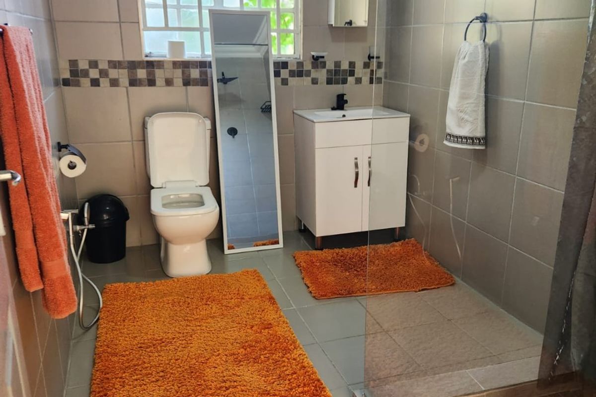 A functional bathroom featuring a vanity cabinet, toilet, and a glass-enclosed shower with neutral wall and floor tiling.