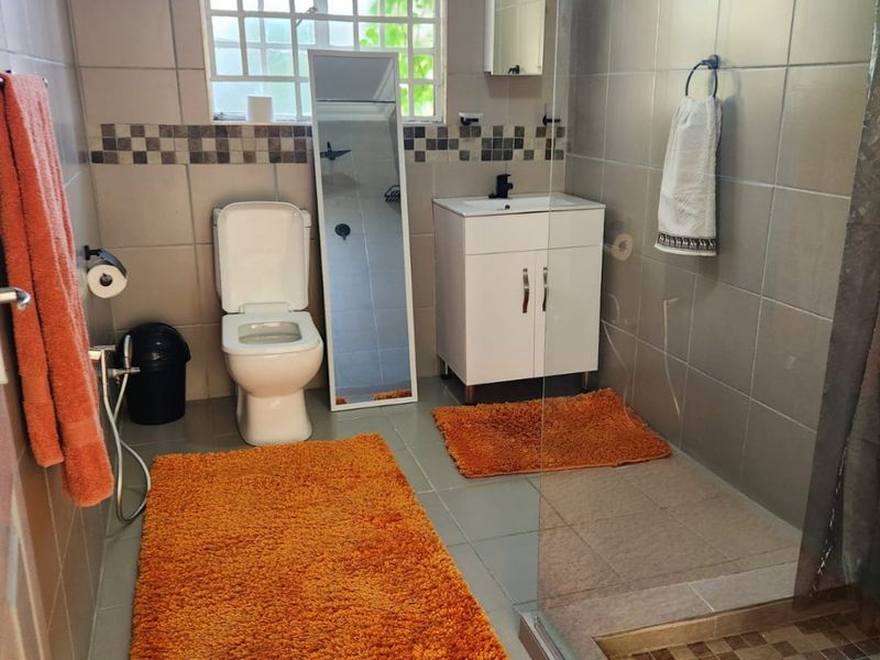 A functional bathroom featuring a vanity cabinet, toilet, and a glass-enclosed shower with neutral wall and floor tiling.