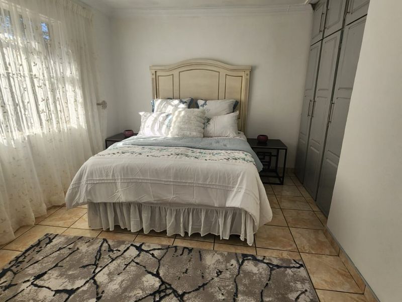 A bedroom featuring tiled flooring, built-in cupboards, and a ceiling fan, offering a functional space with neutral finishes.