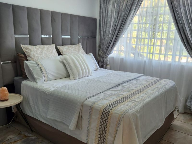 A well-maintained bedroom featuring tiled flooring, a wall-mounted split-system air conditioner, and window security bars with installed curtain tracks.