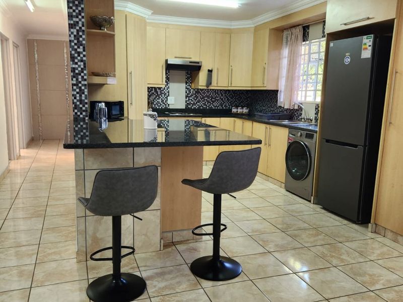 A functional kitchen featuring light wood cabinetry, granite countertops, a mosaic tile backsplash, and ceramic floor tiles with an integrated breakfast bar.
