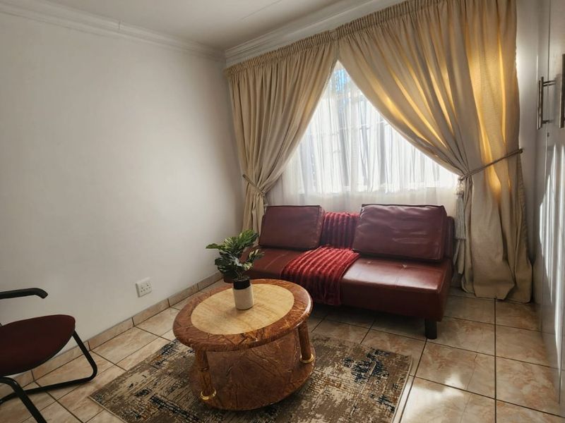 A compact living room featuring ceramic floor tiles, built-in storage, and natural light through a window with draped curtains.
