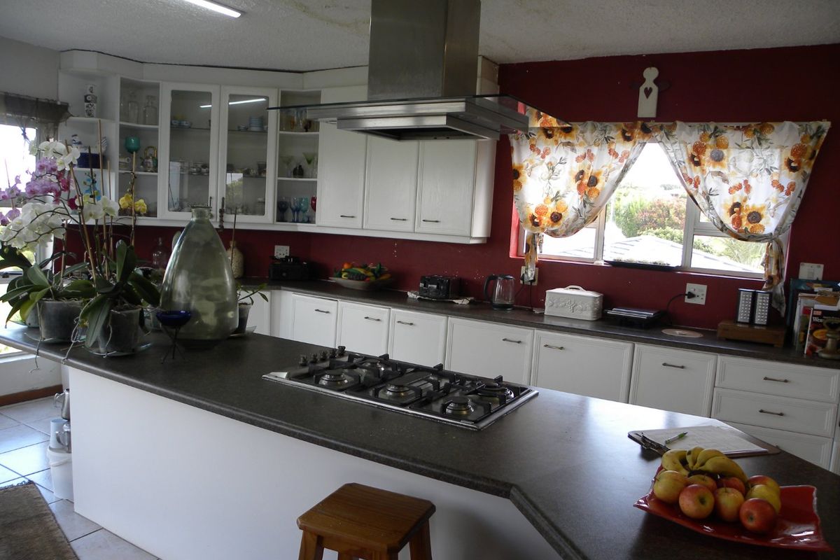 Spacious kitchen featuring white cabinetry, dark stone countertops, a central gas hob with extractor fan, and a breakfast bar area.