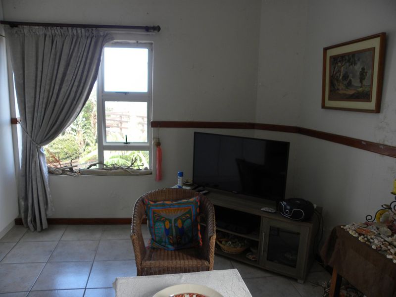 A living room area featuring tiled flooring, a wooden dado rail, and an aluminium window frame with natural light.
