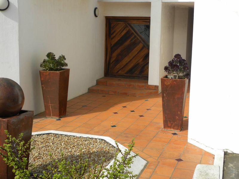 A welcoming entrance area featuring terracotta tiled flooring, a decorative wooden front door, and a built-in water feature.