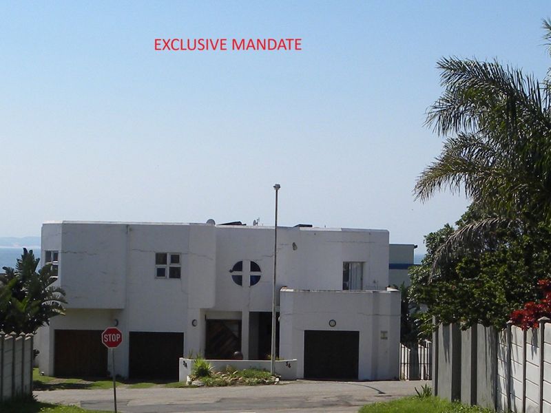Front elevation of a multi-level residential property featuring a double garage, concrete boundary walls, and distinctive circular architectural detailing.