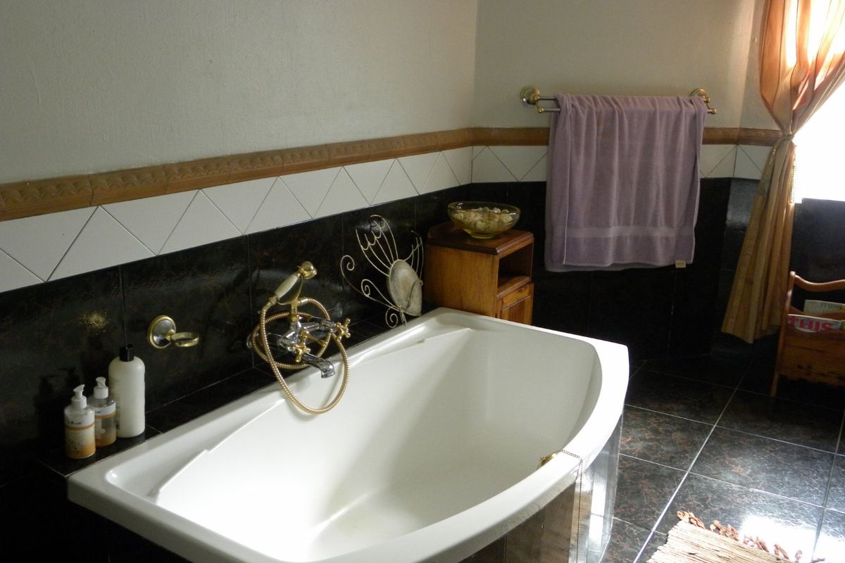 A bathroom featuring a built-in bathtub with gold-tone fixtures, dark tiled flooring, and contrasting wall tiles with a decorative border.
