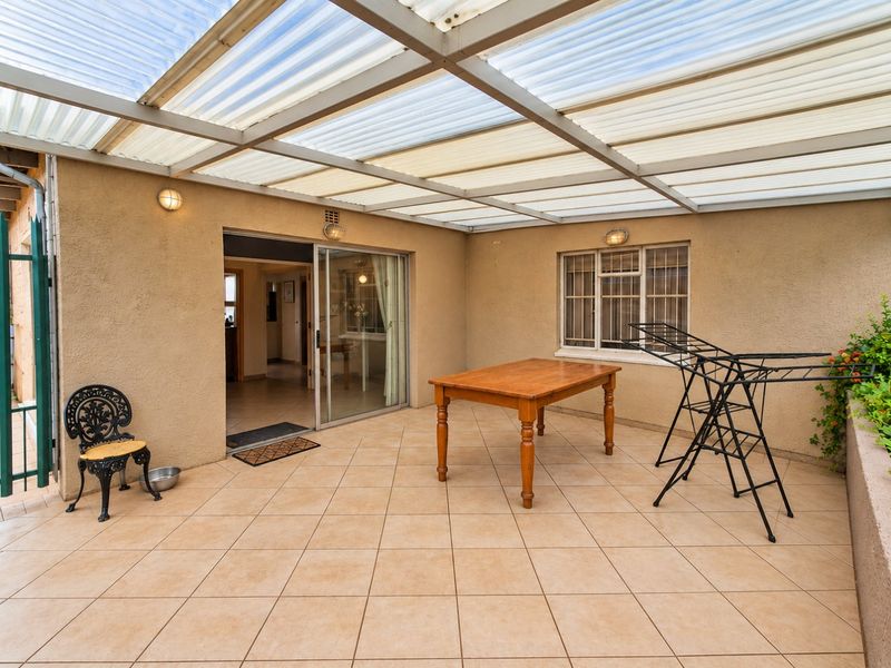 A covered patio area featuring tiled flooring, a corrugated roof structure, and direct access to the interior through a sliding glass door.