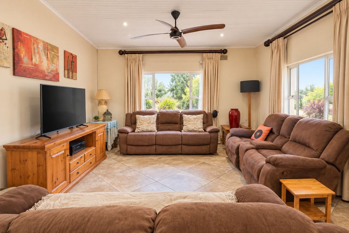 A spacious living room featuring tiled flooring, a ceiling fan, and large windows that provide ample natural light and garden views.