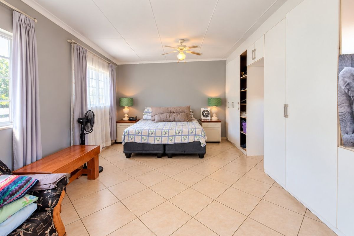 Spacious bedroom featuring neutral tiled flooring, ample built-in cupboard storage, and a central ceiling fan.