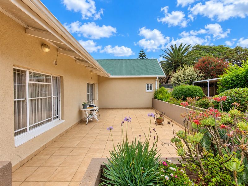 A spacious paved patio area featuring a retaining wall and established garden beds, offering a pleasant outdoor space for relaxation.