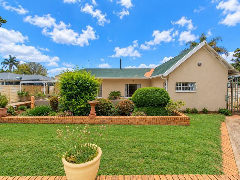 Rear view of the house featuring a landscaped garden, brick retaining wall, and a corrugated metal roof with visible wear.
