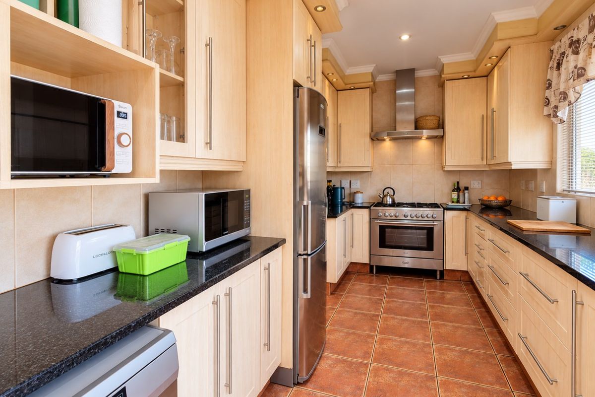 A well-maintained kitchen featuring light wood cabinetry, granite countertops, stainless steel appliances, and tiled flooring with recessed lighting.