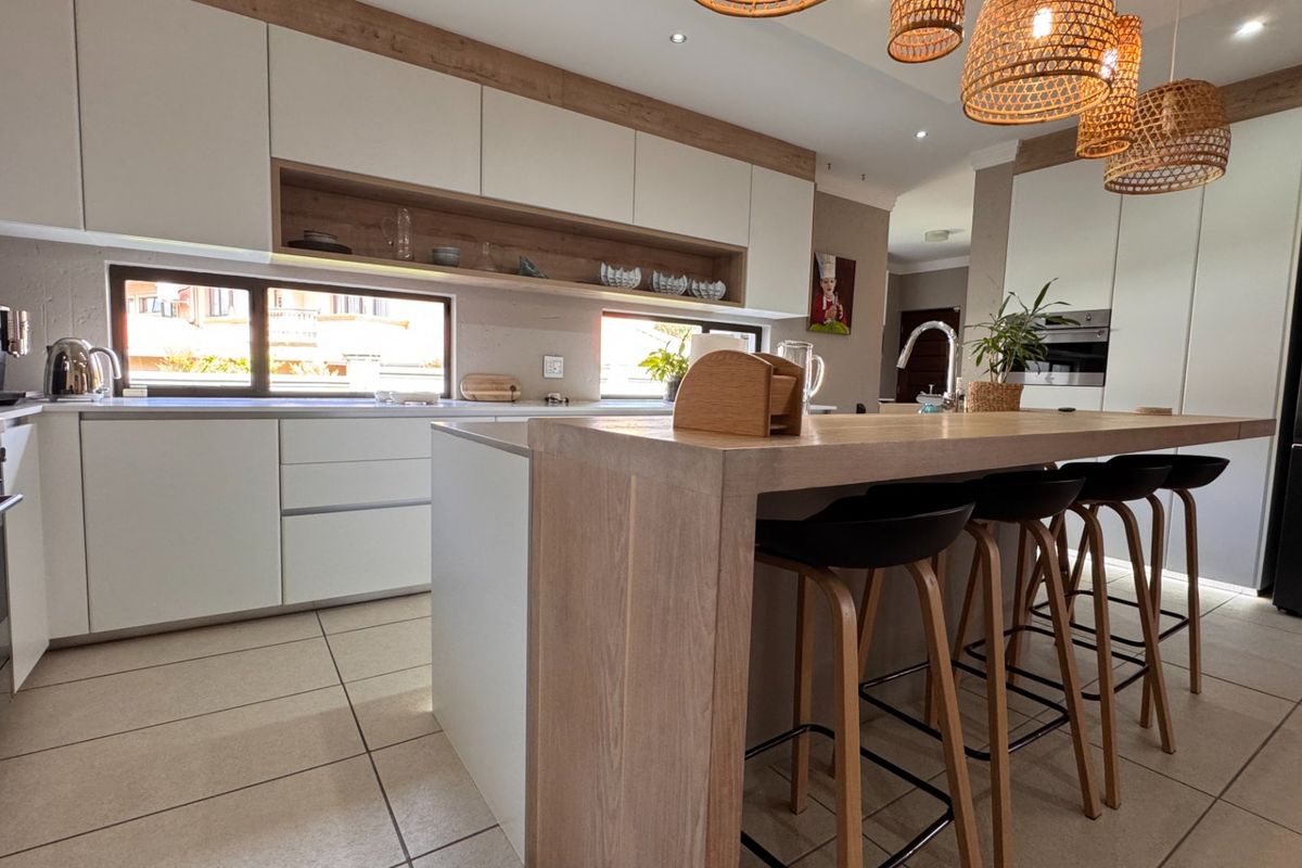 Modern kitchen featuring sleek white cabinetry, a wooden breakfast island, integrated appliances, and tiled flooring with ample natural light.