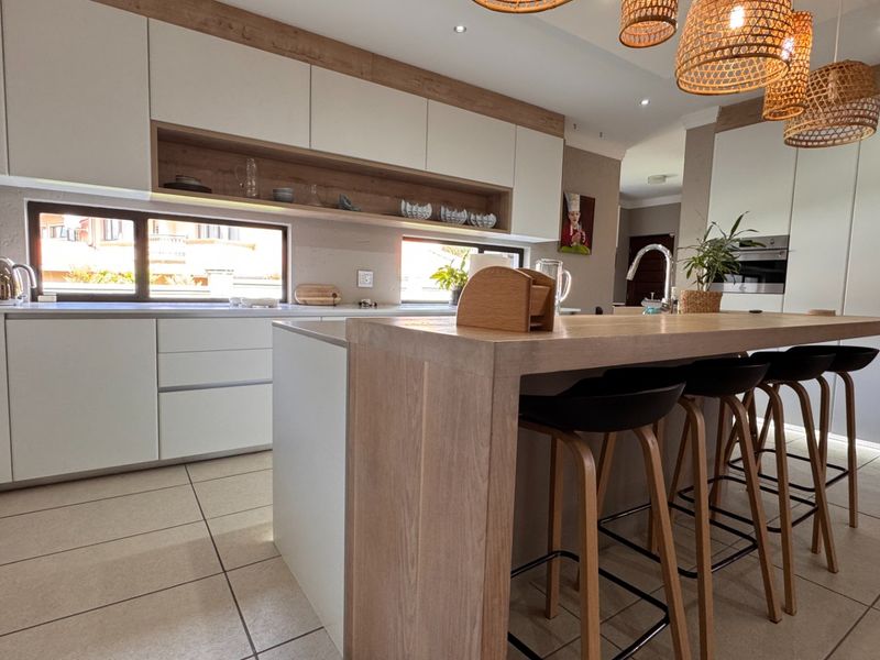 Modern kitchen featuring sleek white cabinetry, a wooden breakfast island, integrated appliances, and tiled flooring with ample natural light.