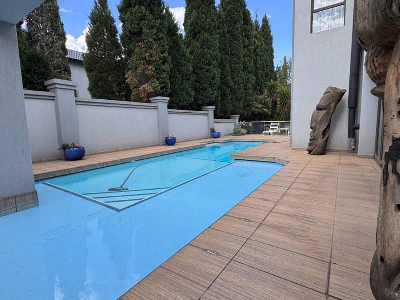A well-maintained swimming pool area featuring a tiled deck, boundary wall, and structural pillars, providing a clean outdoor space.