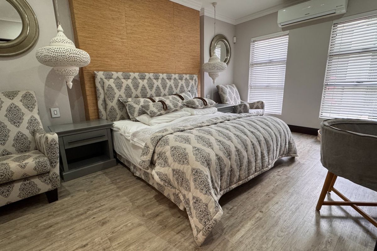A well-maintained bedroom featuring laminate flooring, a timber feature wall, and a wall-mounted air conditioning unit with natural light through venetian blinds.